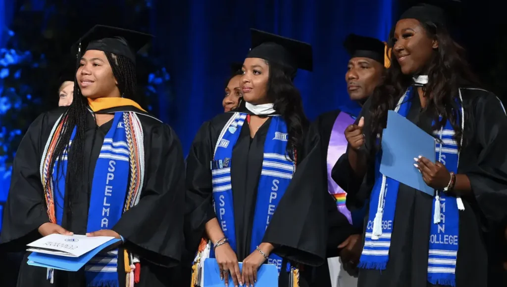 Three HBCU graduates in black caps and gowns wearing blue honor stoles at commencement ceremony