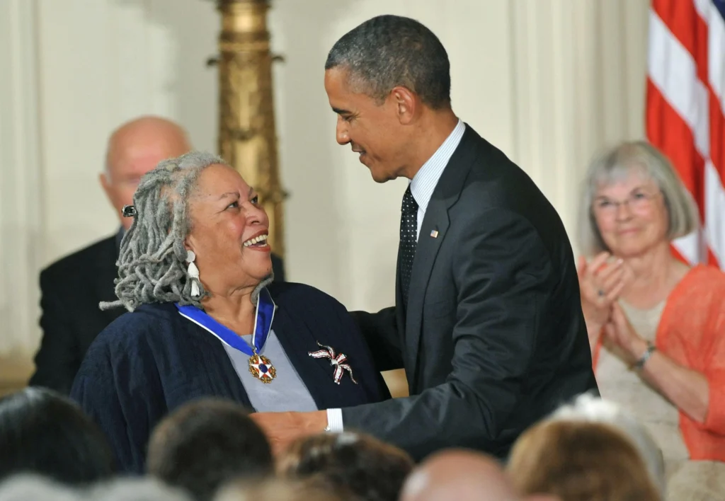 Woman receiving a medal or award from Barak Obama at a ceremonial event with American flag in background