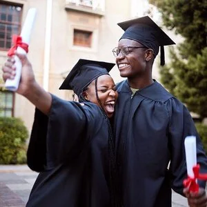 Two HBCU graduates celebrating together in black caps and gowns