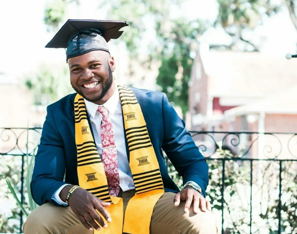 Smiling HBCU graduate in blue cap and gown with gold honor stole